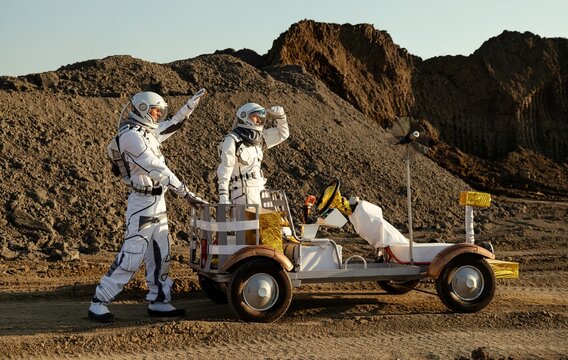 Mars exploration vehicle drives through rocky terrain with astronauts in space suits