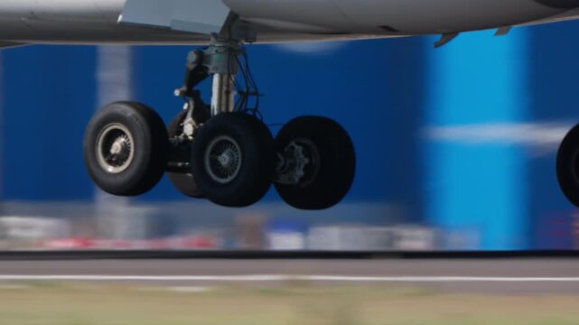 Extreme closeup of commercial passenger jet main landing gear wheels rolling at high speed on airport runway, motion blur background, bright daylight, multiple aircraft visible.