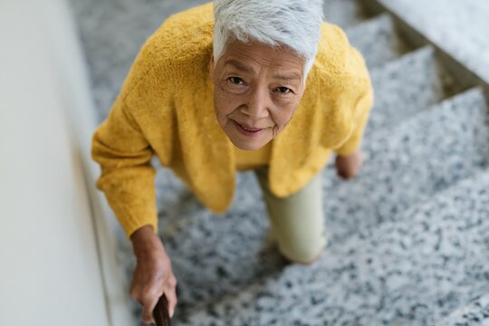 Senior woman climbing stairs holding handrail with cane for fall prevention and mobility care brochure background showing resilience and independent elderly support