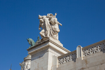 Obraz premium Marble sculptures and architectural details of the Vittoriano monument in Rome, Italy, against a clear blue sky.