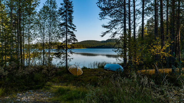 Aerial view of two rowing boats on the shore of a calm lake surrounded by a dense forest of pine and birch trees near Konttainen in Kuusamo, North Ostrobothnia, Finland.