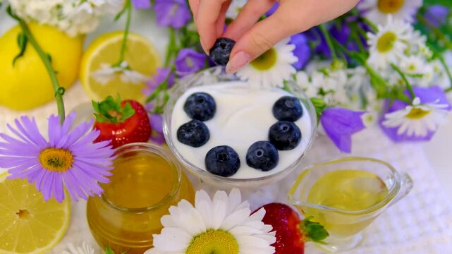 Creamy yogurt is poured into a glass bowl, topped with fresh blueberries and drizzled with golden honey. Bright breakfast scene with chamomile flowers and clean advertising space.