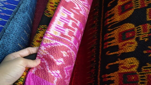 Hand touching rows of colorful traditional Thai silk fabrics, close up , Traditional Isan Thai silk fabrics featuring geometric and elephant patterns.