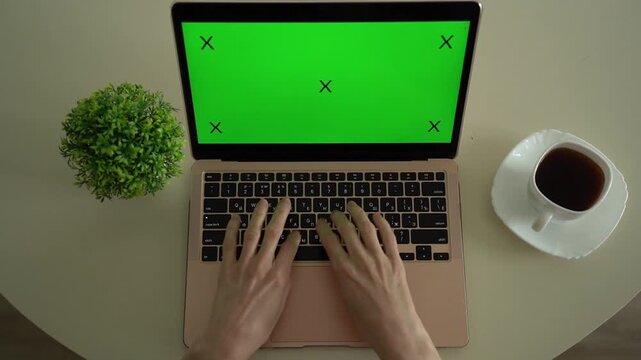 Female hands working on a computer with a green screen at home, with a cup of coffee on the table.