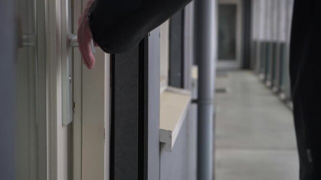 Close up of a man in a dark jacket exiting and locking his modern apartment door on a residential gallery giving it an extra push to close securely