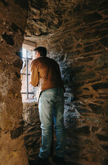 Fototapeta premium A young man looks at the landscape through an ancient window in a castle.