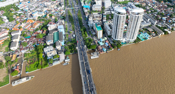 Aerial view of the Chao Phraya River in Bangkok, Thailand, showing traffic on a bridge and buildings along the riverbanks. The brown water indicates potential pollution or sediment.