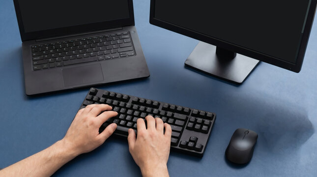 Top view of software developer hands typing on mechanical keyboard with code on laptop and monitor screens