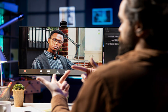 IT admin working from home in videocall with african american coworker, testing programs and systems. Programmer checking code with colleague in online teleconference, sitting at desk in apartment.