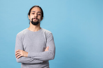 Fototapeta premium Male model with long curly hair posing with confidence in studio, standing with his casual wear against blue background. Young peaceful confident man with self assured attitude.