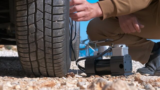 Man inflating a flat tire with a portable air compressor on a dusty road. Close-up of a man's hands connecting a portable air compressor to a car's flat tire valve