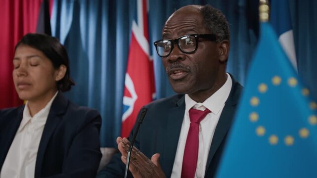 Black adult politician speaking at international summit with European Union flag in foreground. Footage is ideal for global news, political campaigns, and corporate communication zoom in