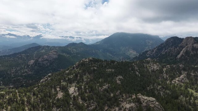 Aerial of heavily forested Rocky Mountain Range in Estes Park Colorado in summer with multiple layers of mountains receding into the distance under cloudy skies