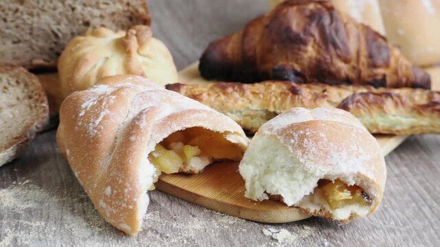 On the table are fresh bread and pastries, apple buns, pies, and croissants. Fresh, warm pastries topped with cheese are displayed in the bakery's display case.