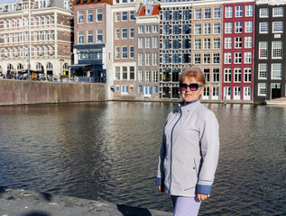 Fototapeta premium An elderly woman wearing sunglasses stands by a canal in the city.