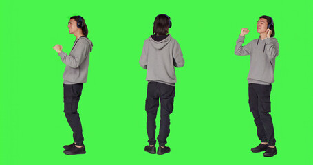 Obraz premium Joyful man does groovy dance moves in studio, feeling funky while he is listening to cool music, with Asian male model smiling and enjoying songs on wireless headset, dancing on green screen.