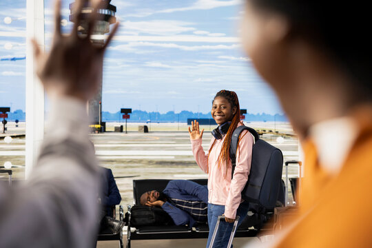 Sad yet proud parents waving goodbye during emotional send-off with their child at the airport, Teenager walking toward gate for boarding, international flight for university abroad, Farewell moment.