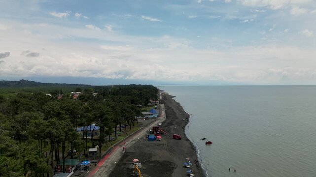 Drone flight along the coastline of Ureki, Georgia, with dark sandy beach, green coastal forest, small boats and the Black Sea stretching to the horizon.