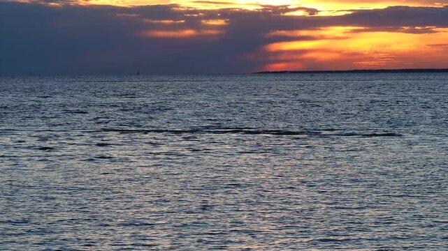 Dramatic golden sunset over a calm sea. Dark clouds gather above the ocean water in the evening. Nature 4K footage for your projects.