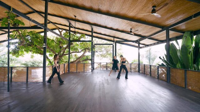 Group of people learning a new choreography during a dance class. Male instructor showing movements to two female students in an open studio