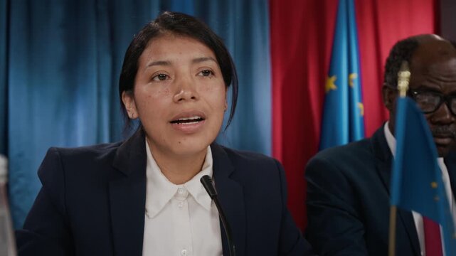 Young Hispanic woman speaking into microphone at political summit. Clip is suitable for news broadcasts, political campaigns, and diplomatic reports