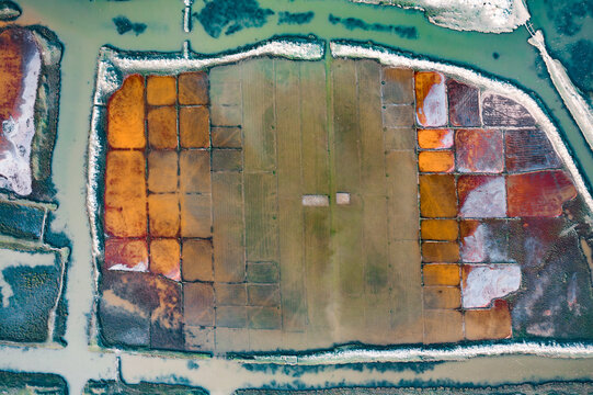 Aerial view of colorful salt pans with geometric patterns and vibrant orange hues surrounded by water channels in Cox's Bazar, Chittagong Division, Bangladesh.