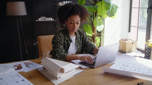African American lady engineer works on laptop by building model