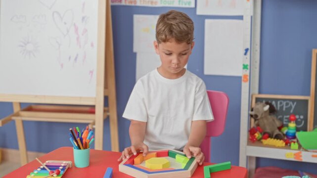 Boy placing colorful wooden shapes on a table, holding a green block while seated in a school building; quiet concentration.