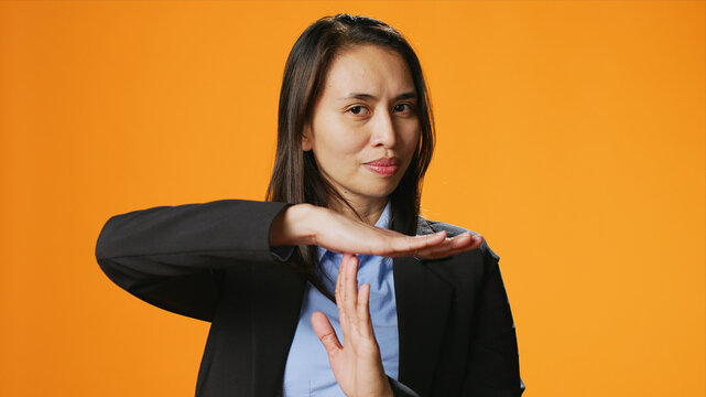 Young woman showing timeout symbol in studio, asking for a break after working hard, standing over background, presenting pause gesture with hands, confident model.