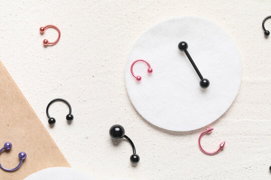 Assorted body piercing jewelry collection with cotton pads on textured background, fashion and self-expression