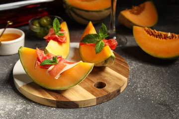 Obraz premium Board of fresh melon pieces with delicious prosciutto and mint leaves on dark background