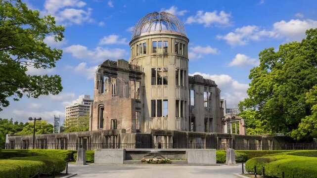 Frontal view of the Hiroshima Peace Memorial in the park. Slow zoom in on the historical Genbaku Dome surrounded by green trees under a blue sky