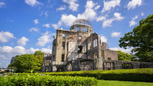 Low angle view of the Hiroshima Peace Memorial Atomic Bomb Dome. Historical ruin surrounded by green foliage under a blue sky with clouds