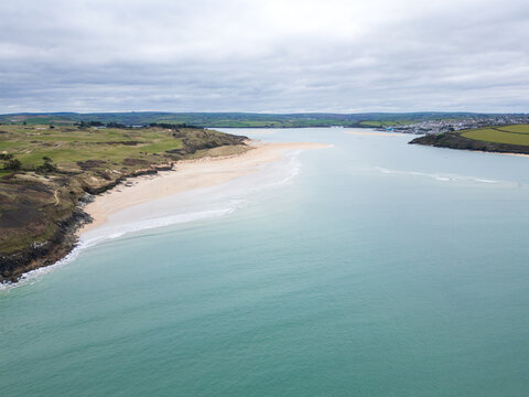 Aerial view of the sandy beach and turquoise waters of the Camel Estuary with rolling green hills and the town of Padstow, Cornwall, United Kingdom.