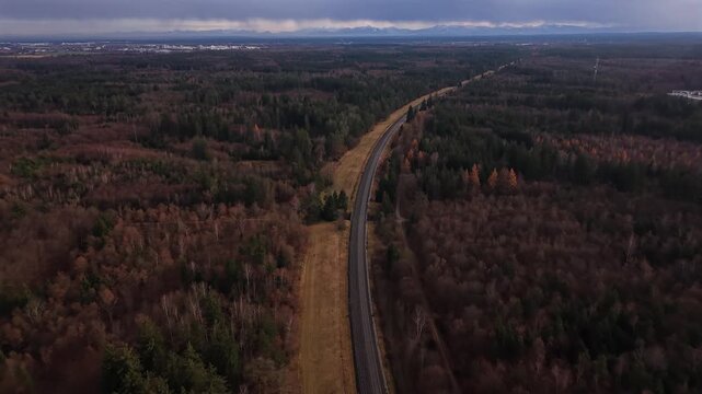 Eine lange Bahnstrecke verlaeuft durch den Perlacher Forst bei Muenchen. Aus der Luft sichtbar fuehrt sie geradewegs Richtung Bayerische Alpen, umgeben von Spaetherbstfarben und beginnendem Winter