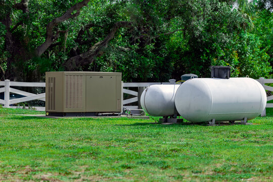 Large standby emergency backup generator connected to white liquid propane gas tanks on green lawn