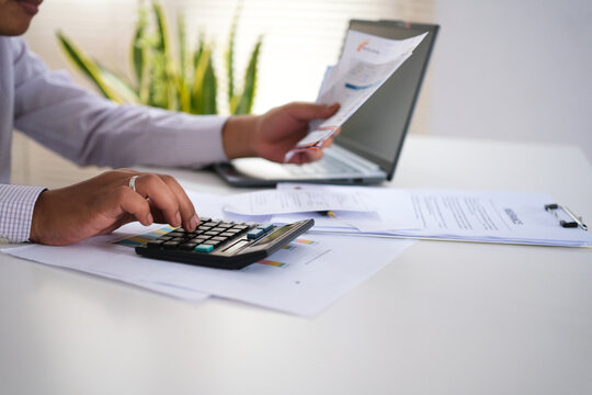 Financial concept, a young businessman holding bills, calculating with a calculator. Financial planning to spend enough of his income to save, pay taxes, and invest.

