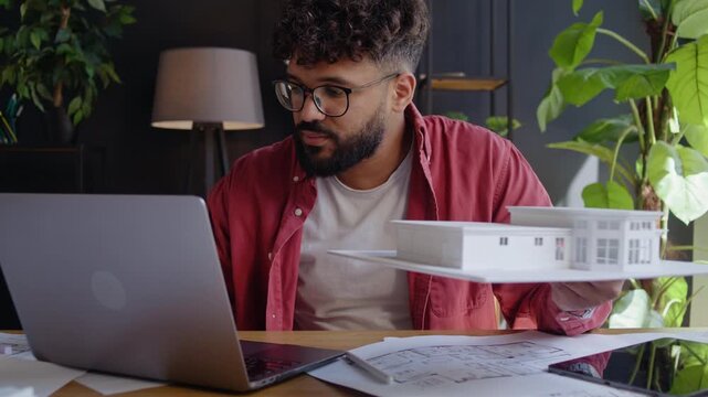 Arab architect records model details near laptop at studio desk