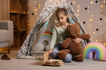 Naklejka premium Cute girl with toy bear reading adventure book at home in evening