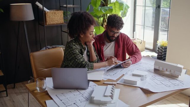 Architects review tablet content and house model at design desk