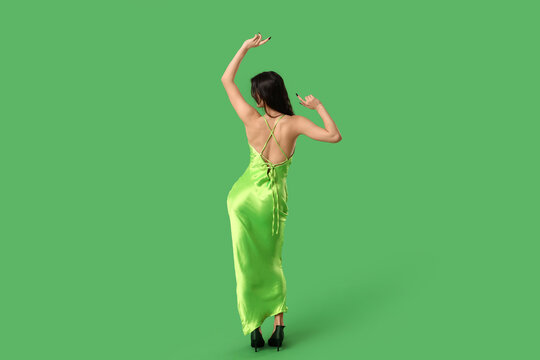 Young woman in stylish green dress dancing on color background, back view