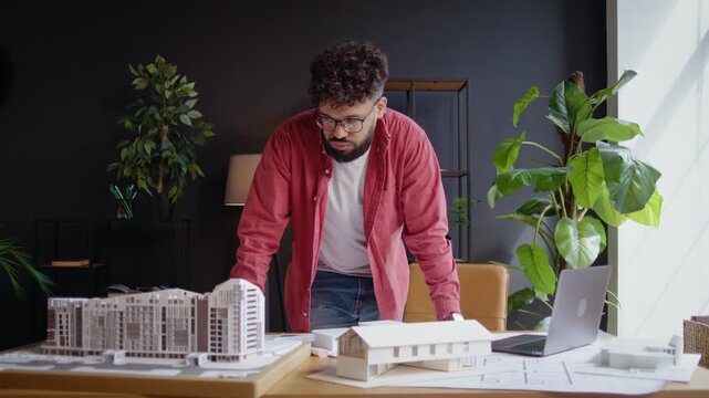 Arab architect reviews scale building models at sunlit desk