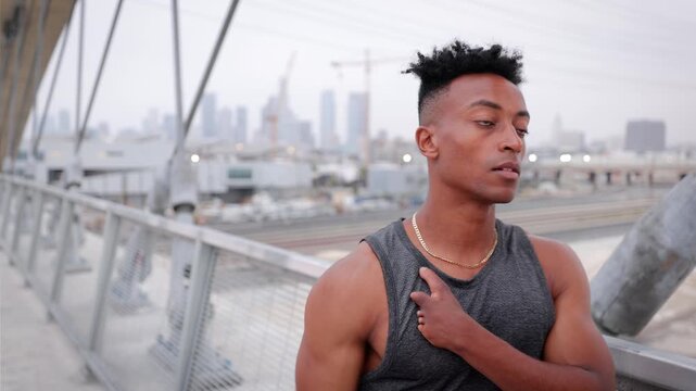 African American man warming up before jogging across the 6th Street Bridge in Los Angeles at dawn on an overcast morning. Downtown LA can be seen in the background. Jogger has a disabled left hand.