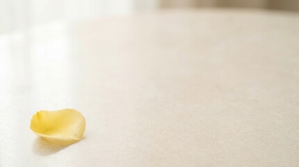 Obraz premium A single yellow rose petal rests on a polished surface, catching the soft light. The scene evokes a sense of delicate beauty and quiet reflection, with a hint of gentle fading or romance.
