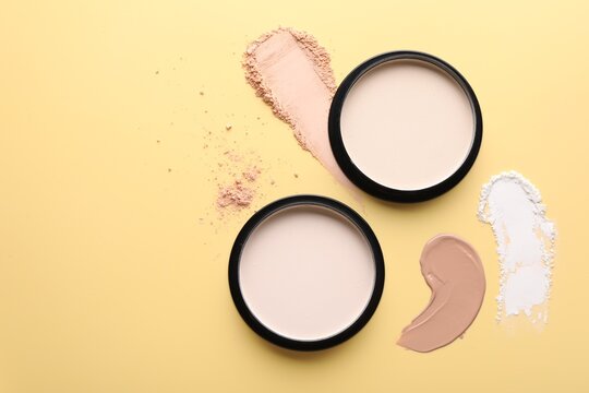 Face powders and liquid foundation on pale yellow background, flat lay. Space for text