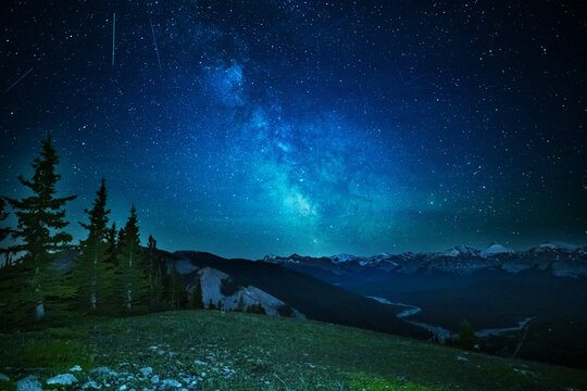 A clear, starry night with the Milky Way in the background, next to a camping tent and the rocky Canadian mountains 