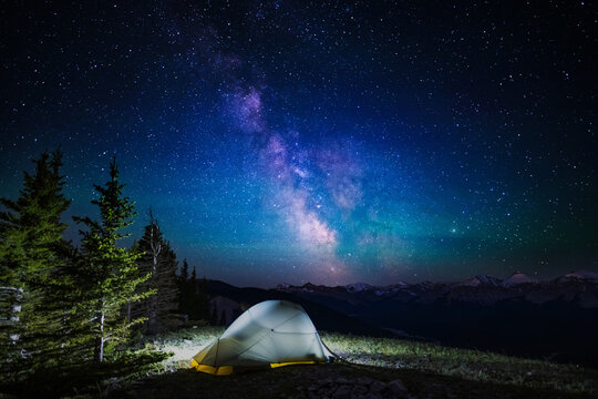 A clear, starry night with the Milky Way in the background, next to a camping tent and the rocky Canadian mountains 
