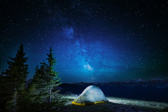 A clear, starry night with the Milky Way in the background, next to a camping tent and the rocky Canadian mountains 