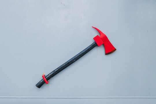 Red emergency fire axe mounted on a gray ship bulkhead wall
