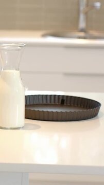 Vertical video: Placing hands moving milk carafe on white counter, prepping with tart pan, pie dish